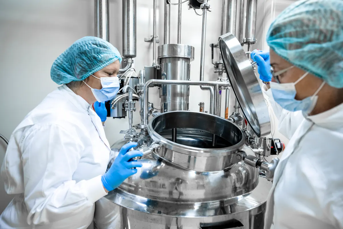 Two workers in protective suits beside an open stainless steel tank